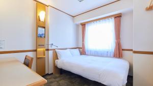Toyoko Inn Fukuoka Tenjin في فوكوكا: غرفة صغيرة بها سرير ونافذة