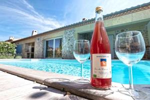 una botella de vino y dos copas junto a la piscina en Belle villa moderne 3 chambres, jardins terrasse piscine, en Durban-Corbières