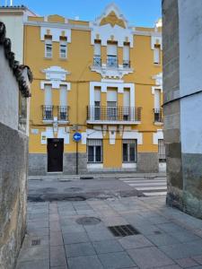 um edifício amarelo com uma porta preta numa rua em Apartamentos Turísticos LOS BARRUECOS em Cáceres