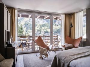 a bedroom with a bed and chairs and a balcony at CERVO Mountain Resort in Zermatt