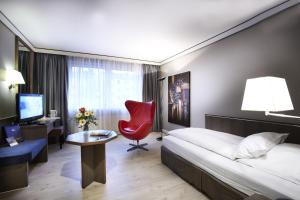デュッセルドルフにあるホテル デュッセルドルフ シティ バイ チューリップ インのベッドと赤い椅子が備わるホテルルームです。