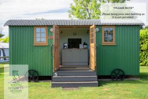 einem grünen Schuppen mit einer Tür und einer Veranda in der Unterkunft Glamping at South Lytchett Manor in Poole
