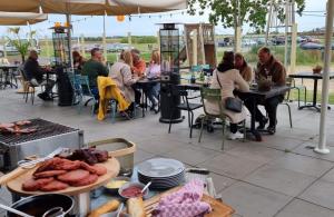 een groep mensen aan tafel in een openluchtrestaurant bij Panoramatent, in de natuur aan zee in Callantsoog