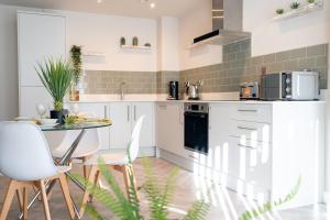 a kitchen with white cabinets and a table and chairs at OLD LISTING Cardiff Bay, Modern Chic 2BR, Free Parking in Cardiff