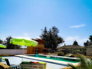 a swimming pool with a green umbrella and chairs at Ferme Sacrée Nature in Ben Slimane