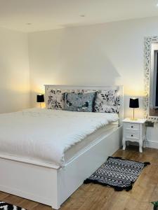 a white bedroom with a large white bed and two lamps at Touchwood in Isleworth