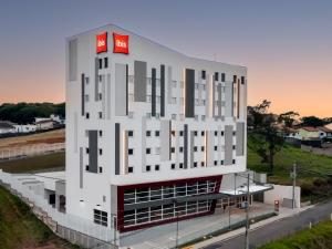 a large white building with two red signs on it at Ibis Aruja in Arujá