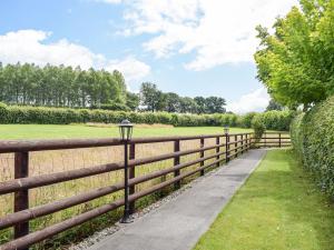 a wooden fence with a sidewalk next to a field at The Lodge At Forbury Cottage in Kimbolton