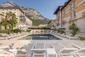 a pool in a courtyard with lounge chairs and a mountain at Grand Hotel Liberty in Riva del Garda