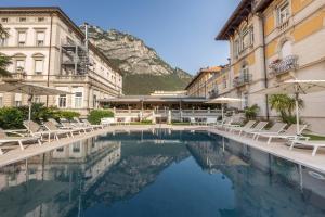 a hotel swimming pool with chairs and a mountain in the background at Grand Hotel Liberty in Riva del Garda