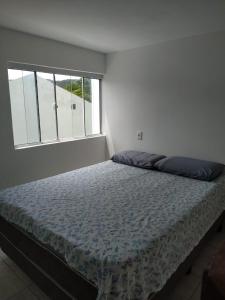Cama en habitación blanca con ventana grande en Loft/APTO em Praia da Pinheira, en Pinheira