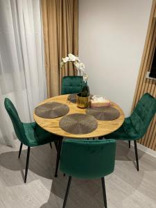 een houten tafel met groene stoelen en een tafel met bloemen erop bij Oxana Apartments - 3 camere - Timisoara in Timişoara