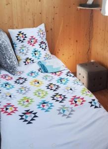 uma cama com um edredão branco com padrões coloridos em A quelques pas du moulin blanc em Brest