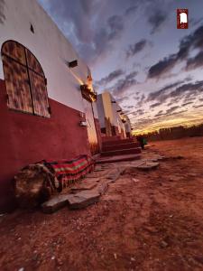 un bâtiment rouge et blanc avec un coucher de soleil en arrière-plan dans l'établissement Gite Agham Azegagh - Timimoun, 