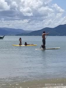 un hombre y dos personas en tablas de surf en el agua en Grandi Pousada Sports - Sambaqui - Chalé Jurerê, Chalé da Mole e 3 Cabanas en Florianópolis