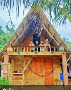 a group of children sitting on the balcony of a thatch house at Titaays Surfers Inn in Baras