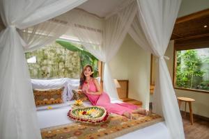 a woman in a pink dress sitting on a bed at Reswaha Villas by Pramana Villas in Ubud