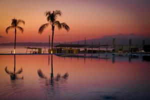 una piscina con palmeras y una puesta de sol en el fondo en Suites @ Aria Ocean, en Nuevo Vallarta 