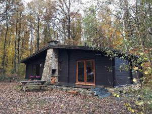 a black cabin in the woods with a bench and trees at Forest Lounge in Petit Mesnil