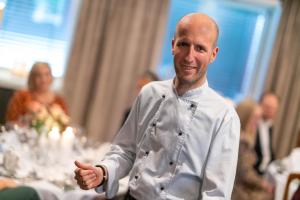 Um homem vestido de chef em frente a uma mesa. em Lampeland Hotel em Lampeland