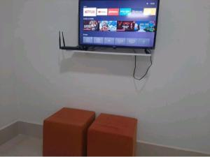 a flat screen tv sitting on a wall with two stools at FlatStudio02 em condomínio residencial na Nova Betânia in Mossoró