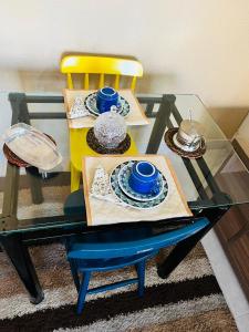a table with a yellow chair and a glass table with plates at Apartamento encantador em salvador in Salvador
