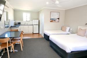 um quarto com duas camas e uma mesa e uma cozinha em Pelican Motor Inn em Merimbula