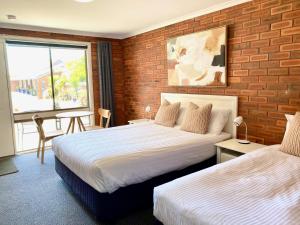 a hotel room with two beds and a brick wall at Pelican Motor Inn in Merimbula