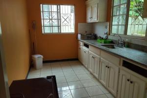 una cocina con armarios blancos, fregadero y ventanas en Unity Villa 3 bedroom with fans Wifi Parking, en Montego Bay