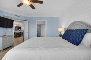 a bedroom with a white bed with blue pillows and a ceiling fan at Heron 507- A Wave From It All in Fort Walton Beach