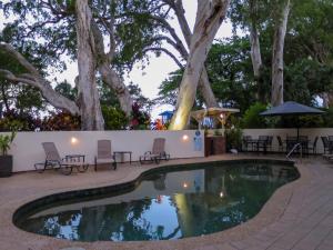 una piscina con sillas, mesas y árboles en Marlin Waters Beachfront Apartments, en Palm Cove