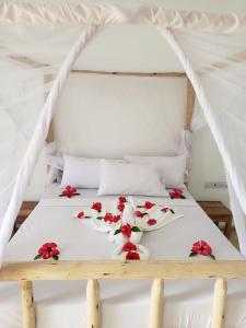 uma cama com lençóis brancos e flores vermelhas em Serenity 2 - Jambiani em Jambiani