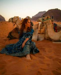 una mujer sentada en el desierto con un camello en Wadi Rum Meteor camp, en Wadi Rum
