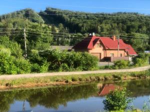 une maison avec un toit rouge à côté d'une rivière dans l'établissement Садиба Мигове, à Myhove