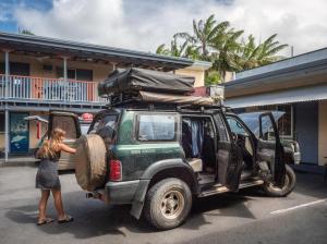 Una mujer está poniendo un neumático en la parte trasera de un jeep verde en Castaways Backpackers Cairns, en Cairns