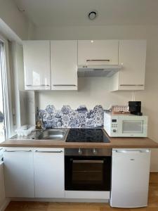 cocina con armarios blancos, fregadero y microondas en Le Marin, à 500m du centre ville, en Dax