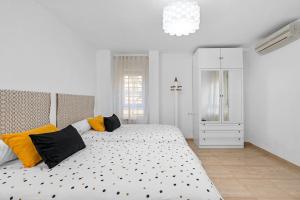 Dormitorio blanco con cama con almohadas amarillas y negras en El rincón de Rosa, en Granada