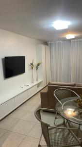 ein Wohnzimmer mit einem Sofa, einem Tisch und einem TV in der Unterkunft Flat Condomínio Beira-Mar in Tamandaré
