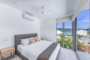 a white bedroom with a bed and a large window at Whitsunday living on Hillcrest in Airlie Beach