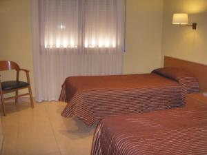 a hotel room with two beds and a chair at Hostal Mallorquines in Riudarenes