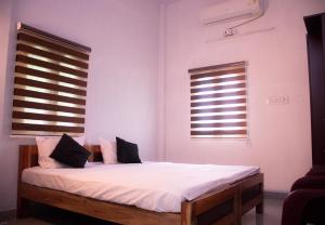1 Schlafzimmer mit einem Bett mit weißer Bettwäsche und 2 Fenstern in der Unterkunft Hotel Padma Shree , Madurai - Near Airport in Madurai