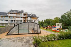 ein Glashaus mit einem Spielplatz vor einem Gebäude in der Unterkunft Baltic Sun Muszelka in Sztutowo