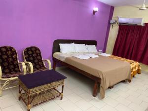 a bedroom with a bed and two chairs and a purple wall at Hotel Samudra Tara in Kovalam