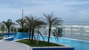 a swimming pool with palm trees and the beach at Apartamento pé na areia in Itanhaém