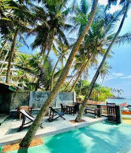 a pool with tables and chairs and palm trees at Praneeth Guest House in Mirissa