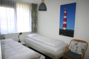 a room with two beds and a chair and a lighthouse picture at Duinroos in Nes