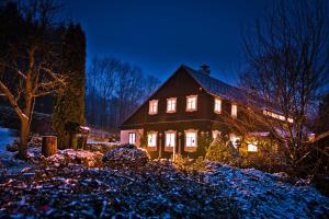 a house with lights on in the snow at night at Penzion pod Železným Vrchem in Chřibská