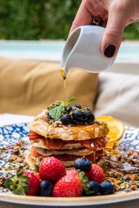 a person pouring syrup onto a stack of pancakes with berries at Casa Nostra Boutique Hotel & Spa in Palermo