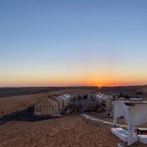 uma vista para um deserto com tendas e um pôr-do-sol em djou luxury desert camp em Merzouga