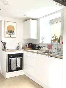 a kitchen with white cabinets and a black dishwasher at Beautiful self-contained Cotswolds Barn in Yatton Keynell